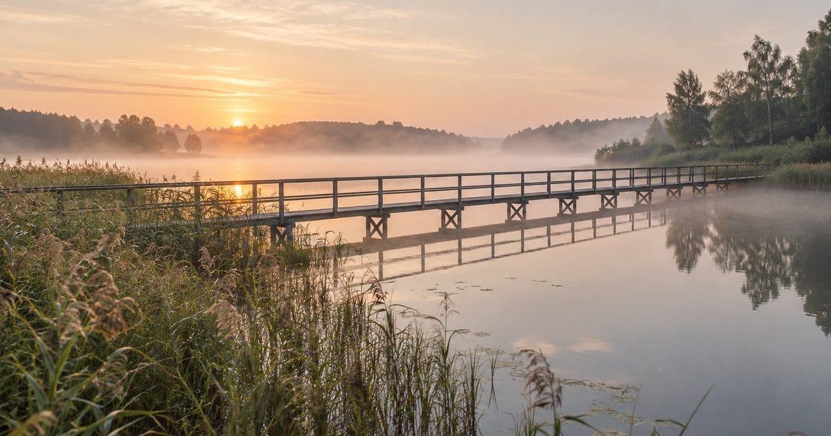 Ilgas medinis tiltas per ramų ežerą ryto rūke