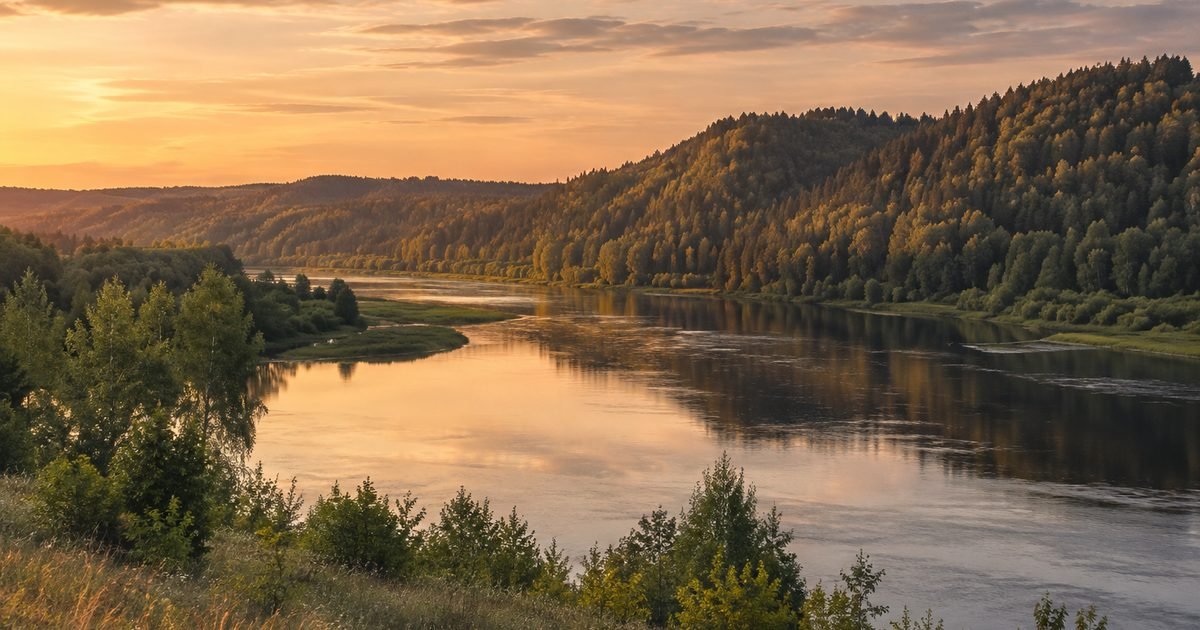 Plati upė po aukštomis miškingomis kalvomis vakaro šviesoje